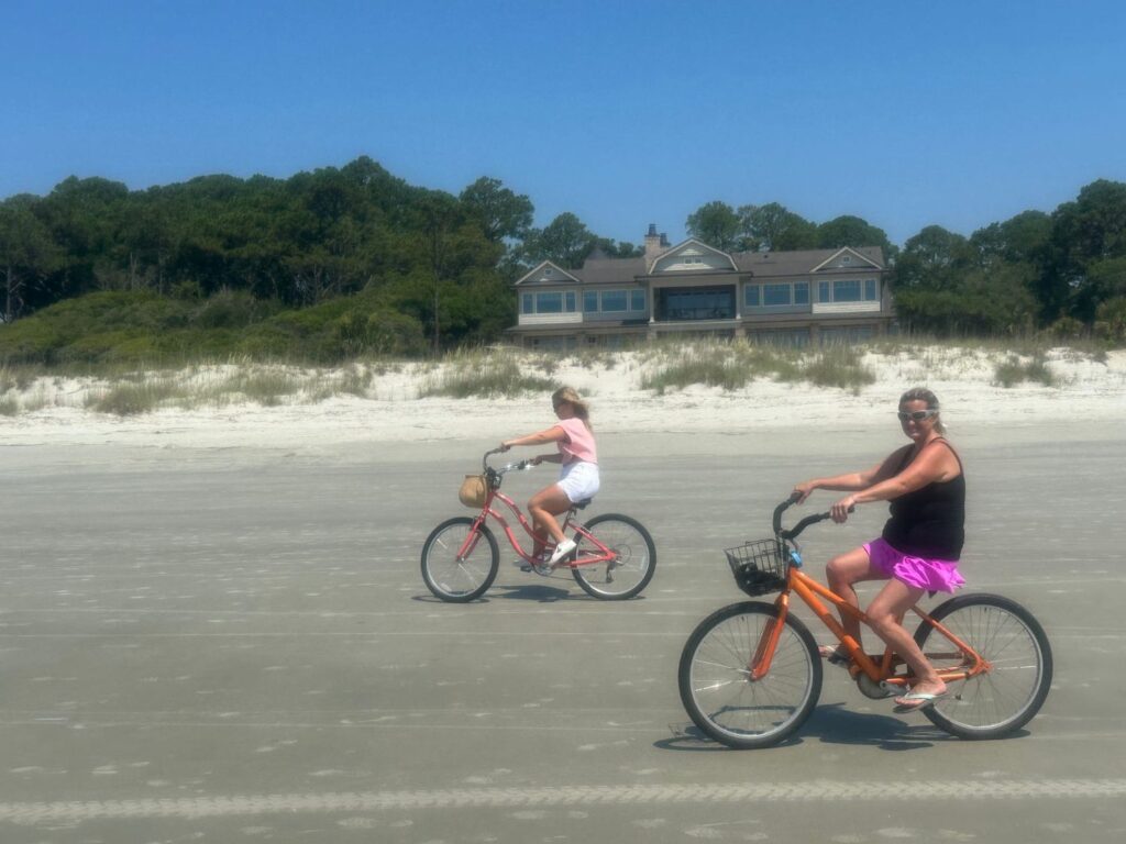 bikes on the beach Two people riding bikes on the beach with a house in the background.