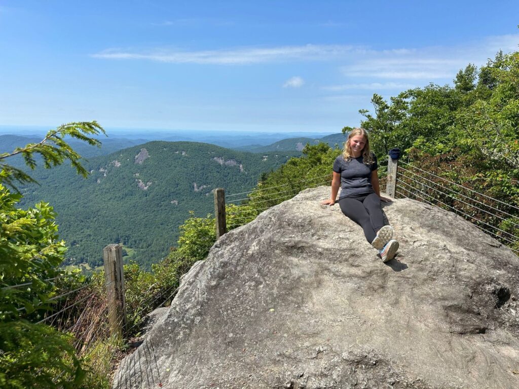 view from the rocks A woman sitting on an outcropping of rocks with mountains in the background.