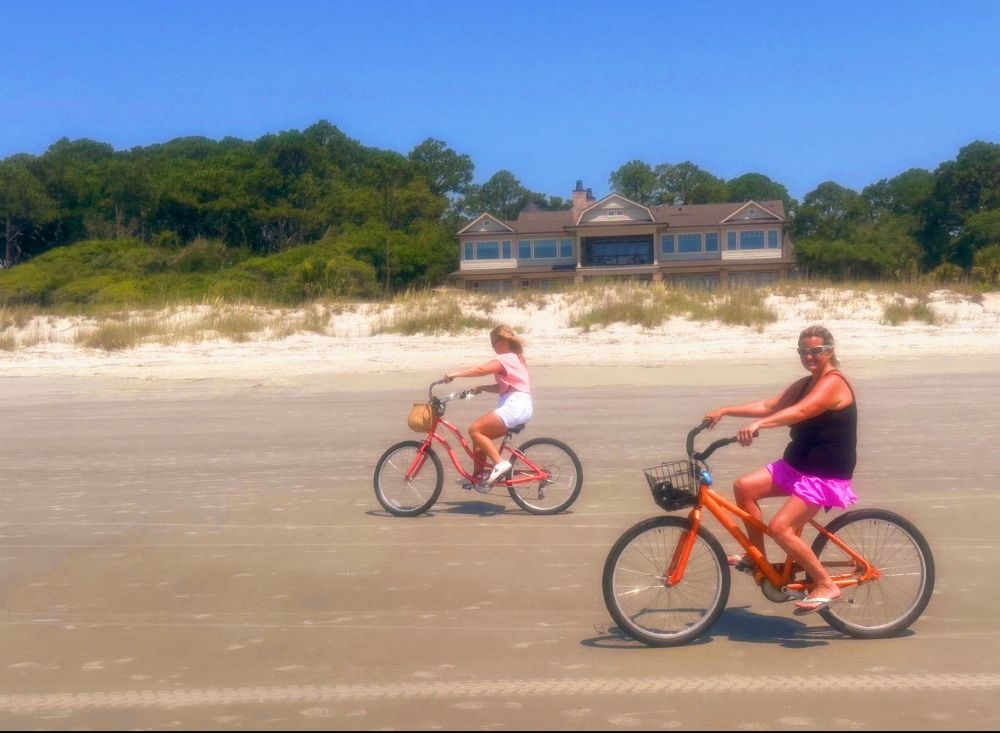 bikes on the beach Two people riding bikes on the beach with a house in the background.